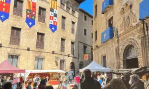 Gente disfruta del mercado medieval de las tres culturas, con puestos y banderas históricas adornando edificios antiguos.