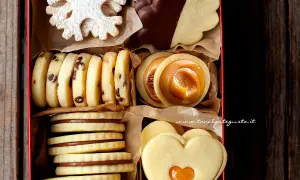 Scatola piena di biscotti al burro: fiocchi di neve, con gocce di cioccolato, ripieni di caramello, a forma di cuore e ricoperti di cioccolato.