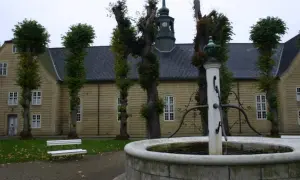 Fontanna przed żółtym budynkiem z wieżą kościelną. Spacerując po **most Niemcy Dania**, można podziwiać architekturę.
