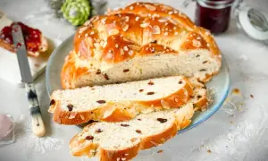 Ein goldbraunes Osterbrot mit Rosinen und Mandelsplittern, perfekt gebacken mit Trockenhefe. Dazu ein Glas Marmelade.