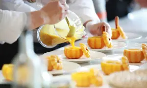 Szef kuchni, pomoc kuchenna kod zawodu, nalewa zupę dyniową do wydrążonych dyń.