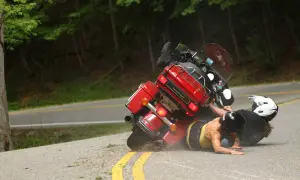 Motocykl leżący na drodze, z dwoma kierowcami na ziemi, w kaskach.