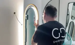Mężczyzna montuje lustro z oświetleniem LED. Widać przewód wychodzący ze ściany, przygotowany do podłączenia.