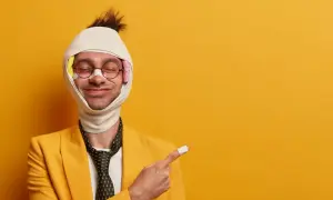 Uomo con benda in testa e cerotto sul dito indica come viene pagato l'infortunio, con un sorriso ironico.