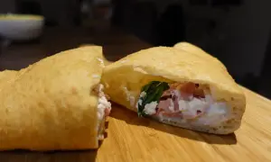 Une pizza frite napolitaine, garnie de ricotta, jambon et basilic, sur une planche en bois.