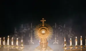 Złota monstrancja z hostią, otoczona płonącymi świecami, symbolizuje obecność Chrystusa. To obraz nawiązujący do 7 sakramentów świętych.