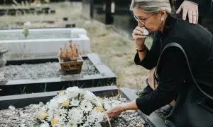 Kobieta płacze przy grobie, kładąc kwiaty. Wsparcie bliskiej osoby i świadomość, że zasiłek pogrzebowy 6000 może pomóc w trudnych chwilach.