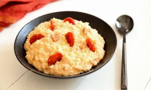 Un crémeux risotto chorizo, garni de rondelles de saucisse épicée, servi dans un bol noir avec une cuillère.