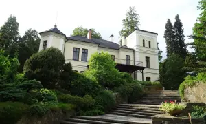 Ein hellgelbes Herrenhaus mit Turm und Balkon, umgeben von üppigem Grün und einer Steintreppe, in Opava, Tschechien.