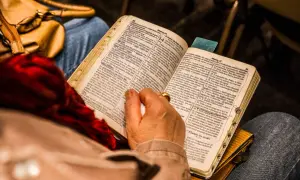 Osoba czyta Biblię, skupiając się na psalm 9. W tle widać torebkę i fragmenty ubrania.