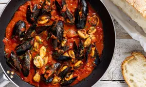 Cozze alla tarantina in padella, un piatto ricco di sapore con cozze succulente in salsa di pomodoro, accompagnate da pane fresco.