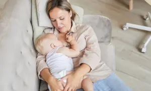 Ciepłe chwile karmienia spod pachy. Mama tuli dziecko, karmiąc je piersią na kanapie.