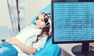 Dziewczynka z czepkiem do eeg leży na łóżku, a na monitorze widać zapis fal mózgowych.