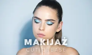 Modelka z błękitnym makijażem oczu w stylu cut crease, z wyraźną kreską i połyskującymi cieniami.