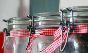 Szklane słoiki z metalowymi klipsami i czerwoną kratkowaną wstążką, gotowe do wyparzania butelek w piekarniku.