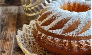 Ciambellone soffice come una nuvola, cosparso di zucchero a velo, adagiato su un centrino di pizzo, su un tavolo di legno rustico.