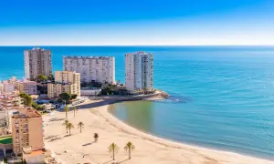 Edificios altos y una playa dorada en el balneario Cullera, con el mar azul brillante de fondo.
