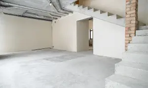 Wnętrze domu w stanie deweloperskim. Betonowe schody, ściany z tynkiem, widoczne instalacje i przewody.