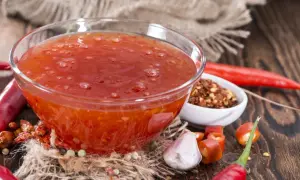 En skål med söt chili sås omgiven av färska och torkade chilifrukter, vitlök och pepparkorn.