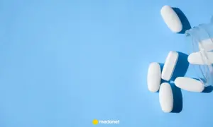 Białe tabletki, jakby wypadły z butelki, leżą na niebieskim tle. Może to być pomoc w walce z bólem, jak np. oxydolor.