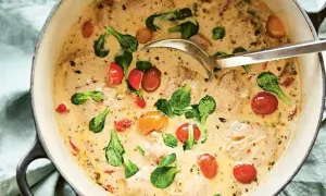 En krämig provensalsk kycklinggryta med körsbärstomater och gröna blad i en gjutjärnsgryta.