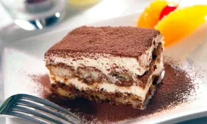 En bit krämig tiramisu, pudrad med kakao, serveras med frukt. Perfekt som dryck till tiramisu är kaffe eller en söt dessertvin.