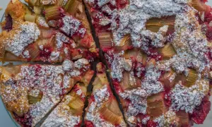 Pyszne ciasto jogurtowe z rabarbarem i malinami, posypane cukrem pudrem. Idealne na letnie popołudnie.
