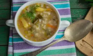 Miseczka zupy z kaszą, ziemniakami i koperkiem, obok łyżka.