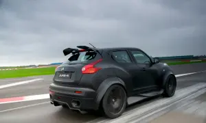 Czarny Nissan Juke-R z masywnym spojlerem pędzi po torze wyścigowym, zostawiając za sobą smugę rozmytych linii.
