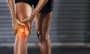Eine Person hält ihr Knie, das rot leuchtet, um **Schmerzen unter der Kniescheibe** zu symbolisieren.