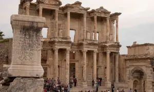 Imponerande ruiner i Efesos, Turkiet, med en antik pelare med inskriptioner framför den storslagna fasaden.