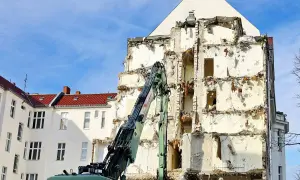Koparka pracuje przy rozbiórce budynku, odsłaniając jego zniszczoną konstrukcję.