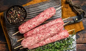 Surowe kofty wołowe na patyczkach, gotowe do grillowania, obok miseczki z pieprzem i gałązki tymianku.