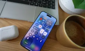 Na ekranie telefonu widać włączony tryb samolotowy. Obok leżą słuchawki, laptop i filiżanka kawy.