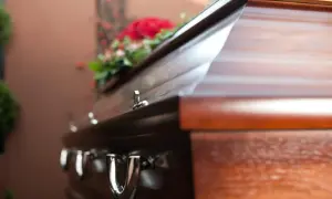 Drewniana trumna z kwiatami, gotowa do pochówku. Rodzina rozważa zwrot kosztów za pomnik.