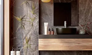 Modern bathroom vanity ideas featuring a floating wood shelf, dark vessel sink, and marble walls. A tall plant adds a natural touch.