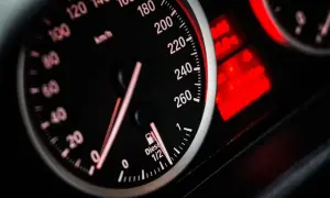 Velocímetro de coche con aguja marcando 120 km/h. El indicador de combustible marca casi lleno. Las luces de advertencia rojas brillan.