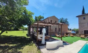 Un'oasi di relax a Poggio San Romualdo: piscina, prato verde, pergolato con divani e lettini prendisole.