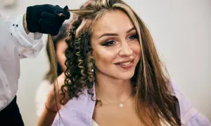 Fryzjerka tworzy loki na włosach z **chunky highlights**. Uśmiechnięta kobieta z makijażem i kolczykiem w wardze.