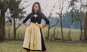 Junge Frau im Dirndl mit einer hellgelben Dirndlschürze aus Leinen, die im Freien steht.