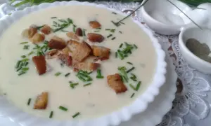 Kremowa zupa porowa z grzankami i szczypiorkiem w białej misce.