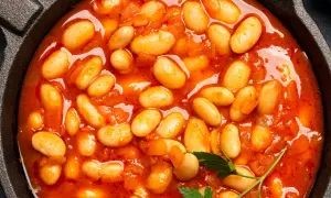 Gęsta, aromatyczna fasolka po bretońsku w sosie pomidorowym, podana w żeliwnym naczyniu.