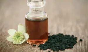 Naturalny olejek z czarnuszki na twarz, w szklanej buteleczce, obok nasion i kwiatu czarnuszki.