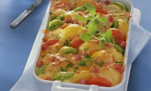 Herzhaftes Kartoffel Lauch Gratin mit Tomaten und Speck, überbacken mit goldbraunem Käse und garniert mit frischen Kräutern.