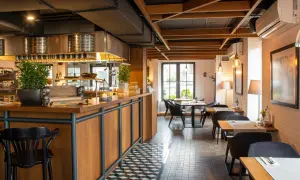 Wnętrze restauracji Magiel: drewniany bar, czarne krzesła, stoliki z białymi obrusami i nowoczesne oświetlenie tworzą przytulną atmosferę.