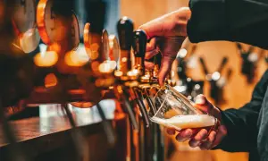 Mano che versa birra da una spillatrice, creando una schiuma perfetta. La spillatura alla tedesca è un'arte.