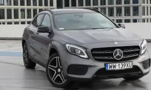 Szary Mercedes GLA 220 z polskimi tablicami rejestracyjnymi stoi na parkingu przed nowoczesnym budynkiem.