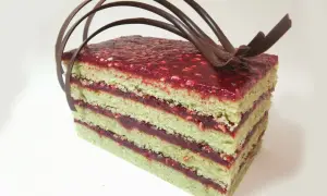 Gâteau pistache framboise mascarpone, une tranche aux couches vertes et rouges, garnie de chocolat.