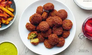 Talerz pełen chrupiących kuleczek, które są odpowiedzią na pytanie: co to jest falafel? Obok sos i frytki.