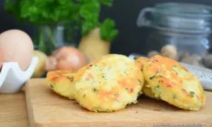 Goldbraune Macaire Kartoffeln, frisch zubereitet, liegen auf einem Holzbrett. Zutaten wie Eier und Petersilie sind im Hintergrund zu sehen.